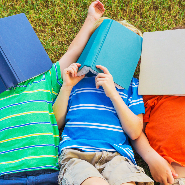 three children laying on the grass with books over their faces