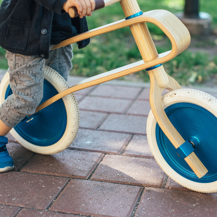 Image of a young child sitting on a wooden balance bike on a brick path