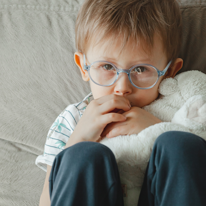young boy sitting on sofa with knees up by chest, hands in mouth looking sad. Comforted by a white plush toy