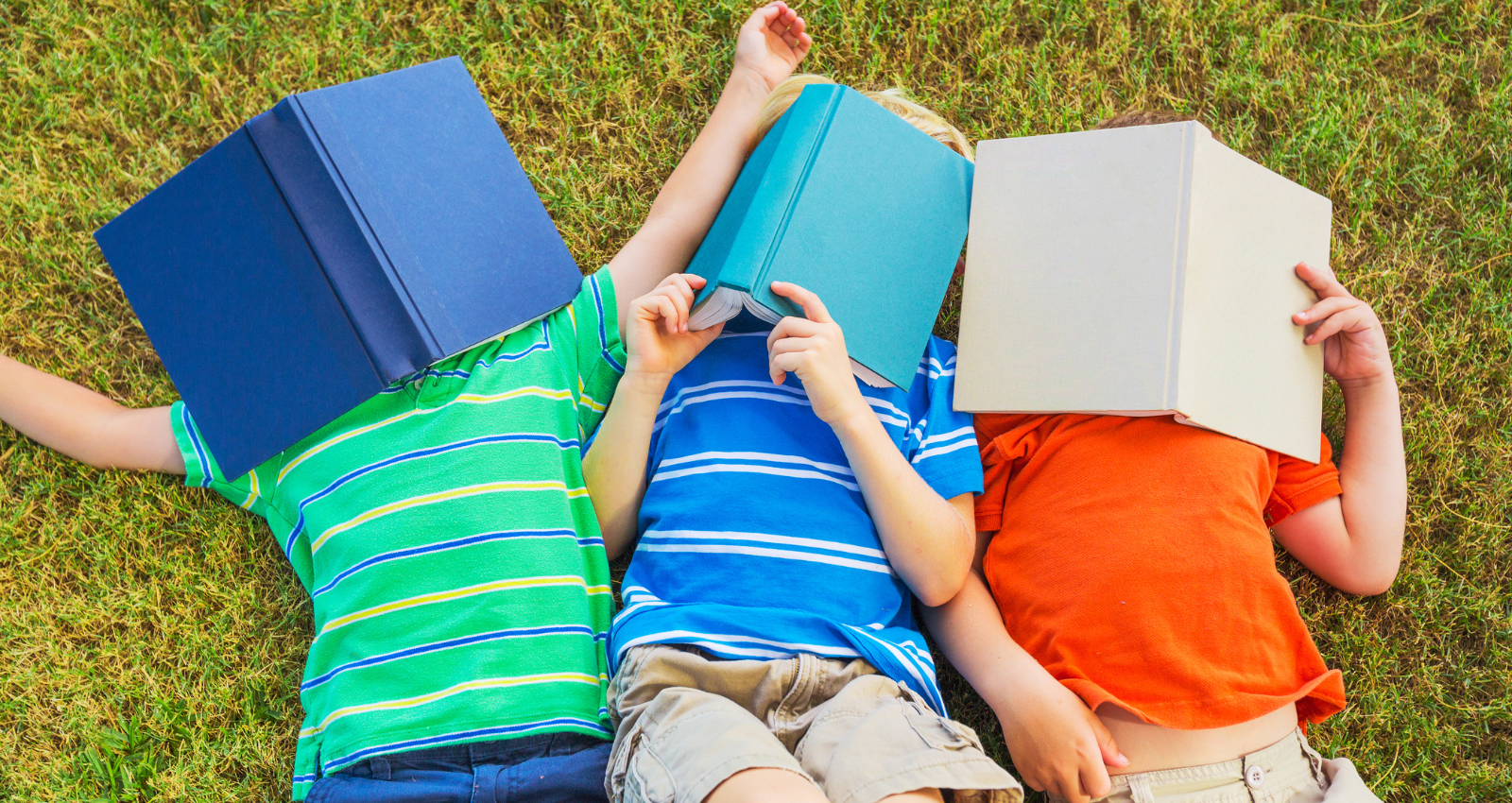 three children laying on the grass with books over their faces