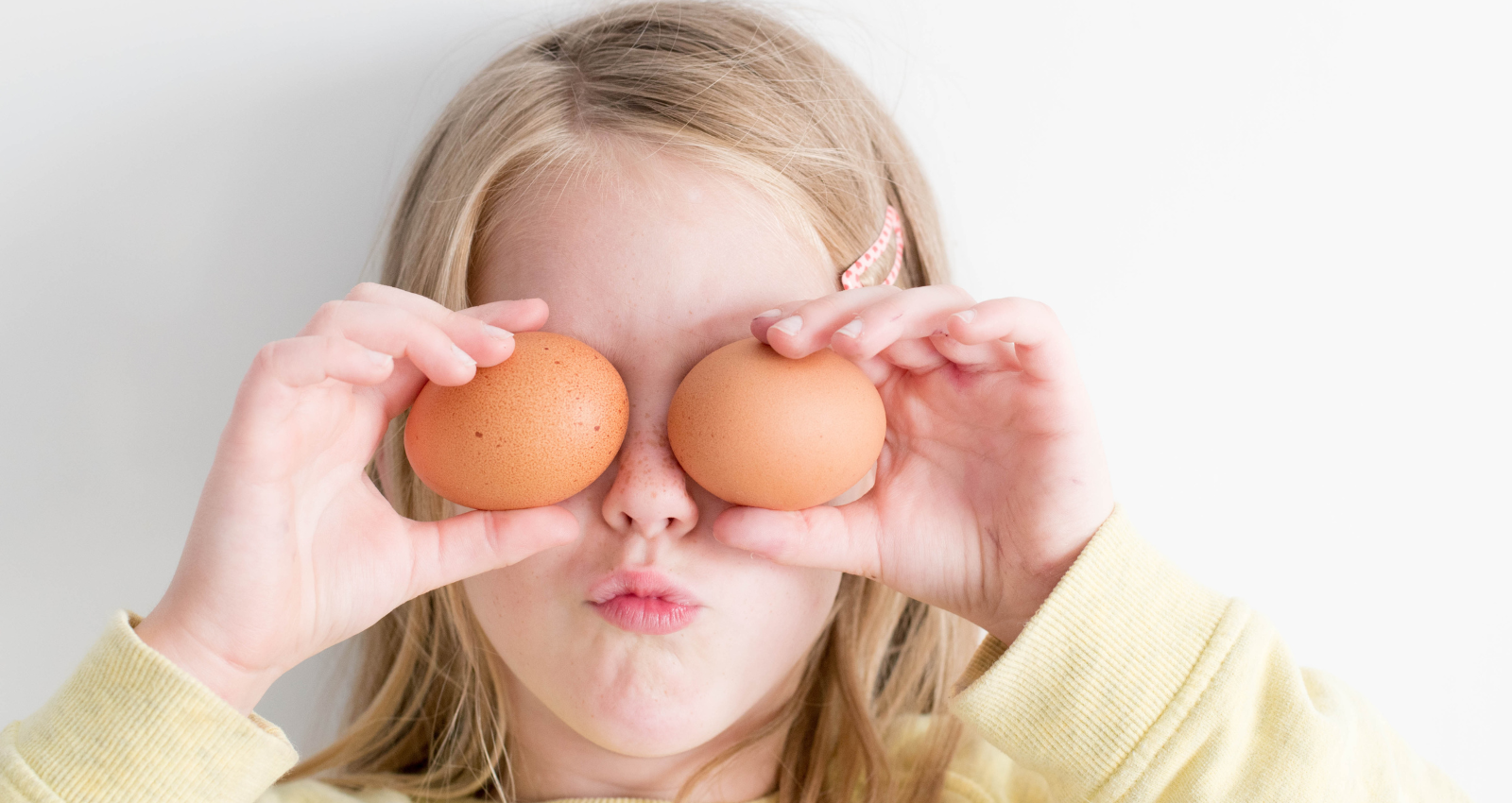 Young girl holding two eggs up in front of her face in a playful gesture