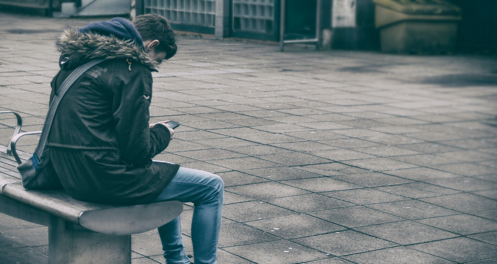 boy sitting on a bench bent over looking at their mobile phone