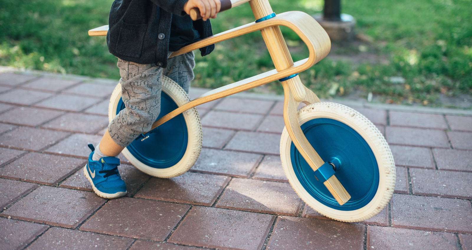 Image of a young child sitting on a wooden balance bike on a brick path
