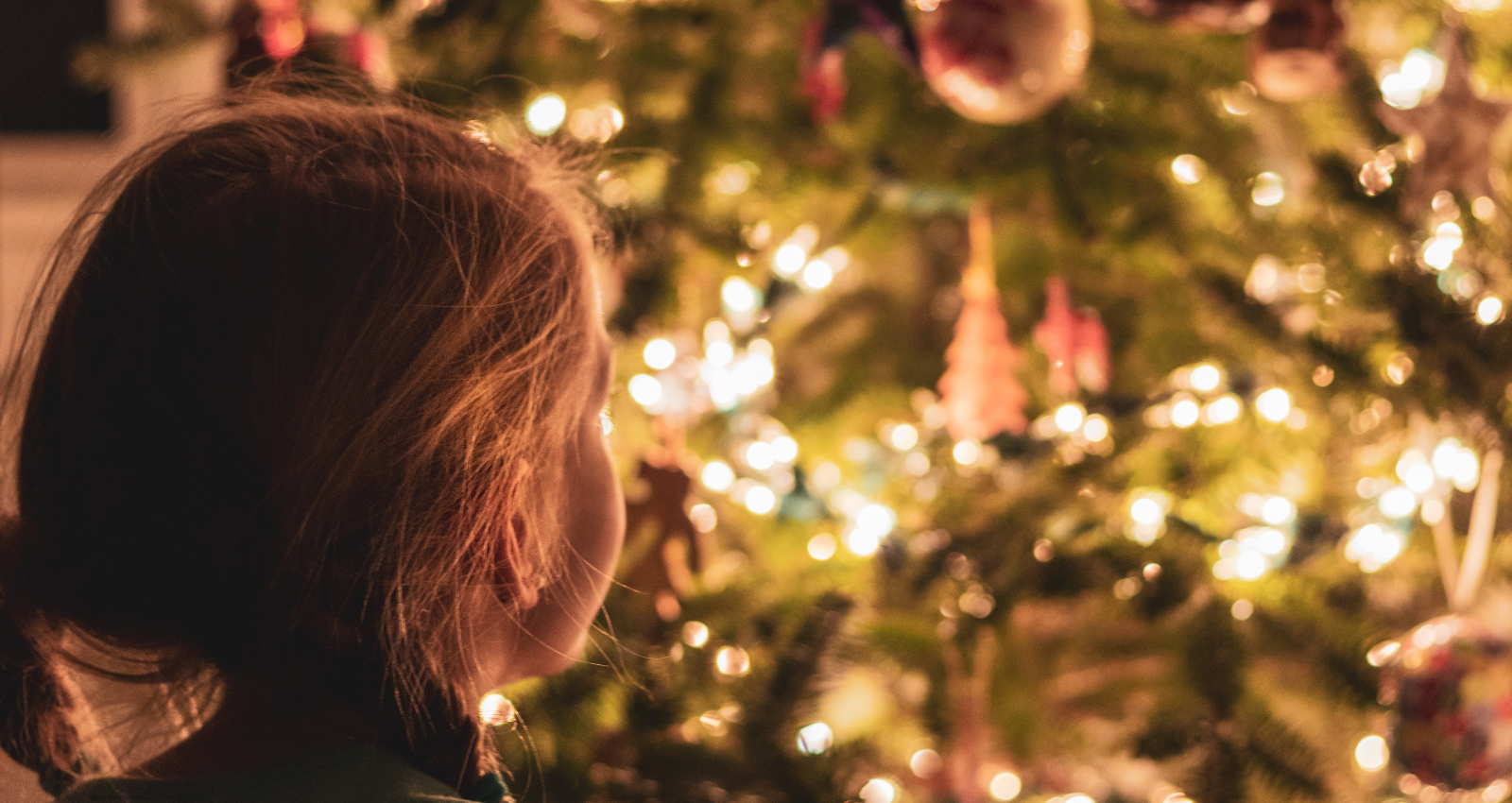 young girl standing in front of a lit up Christmas tree