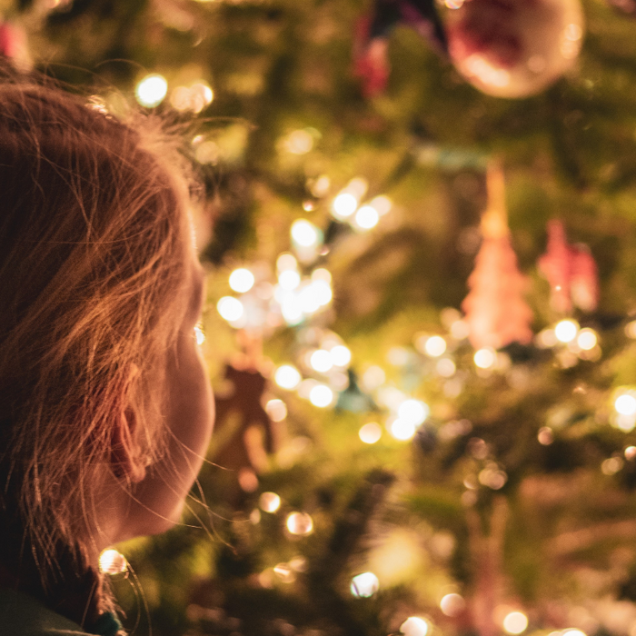 young girl standing in front of a lit up Christmas tree