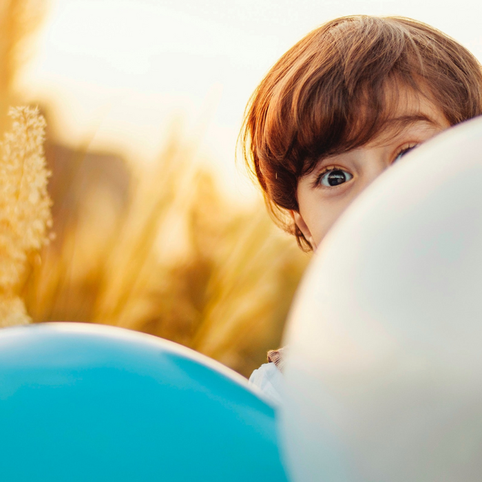 boy peeking over two balloons in a wheat field